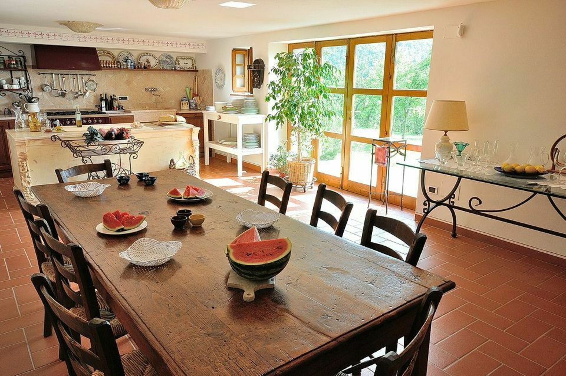 A spacious kitchen with a wooden dining table set for four, featuring a large bowl of watermelon and plates of food.