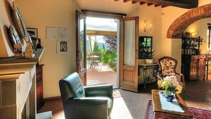 A spacious living room with a leather chair, a wooden table with a vase of flowers, and a view of a garden through an open door.