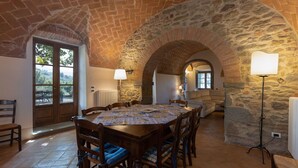 A dining area with a stone arch, a table with chairs, and a view through a door. - Wonderful private villa with private pool, WIFI, A/C, TV, patio, panoramic view, close to Cortona (Cegliolo)