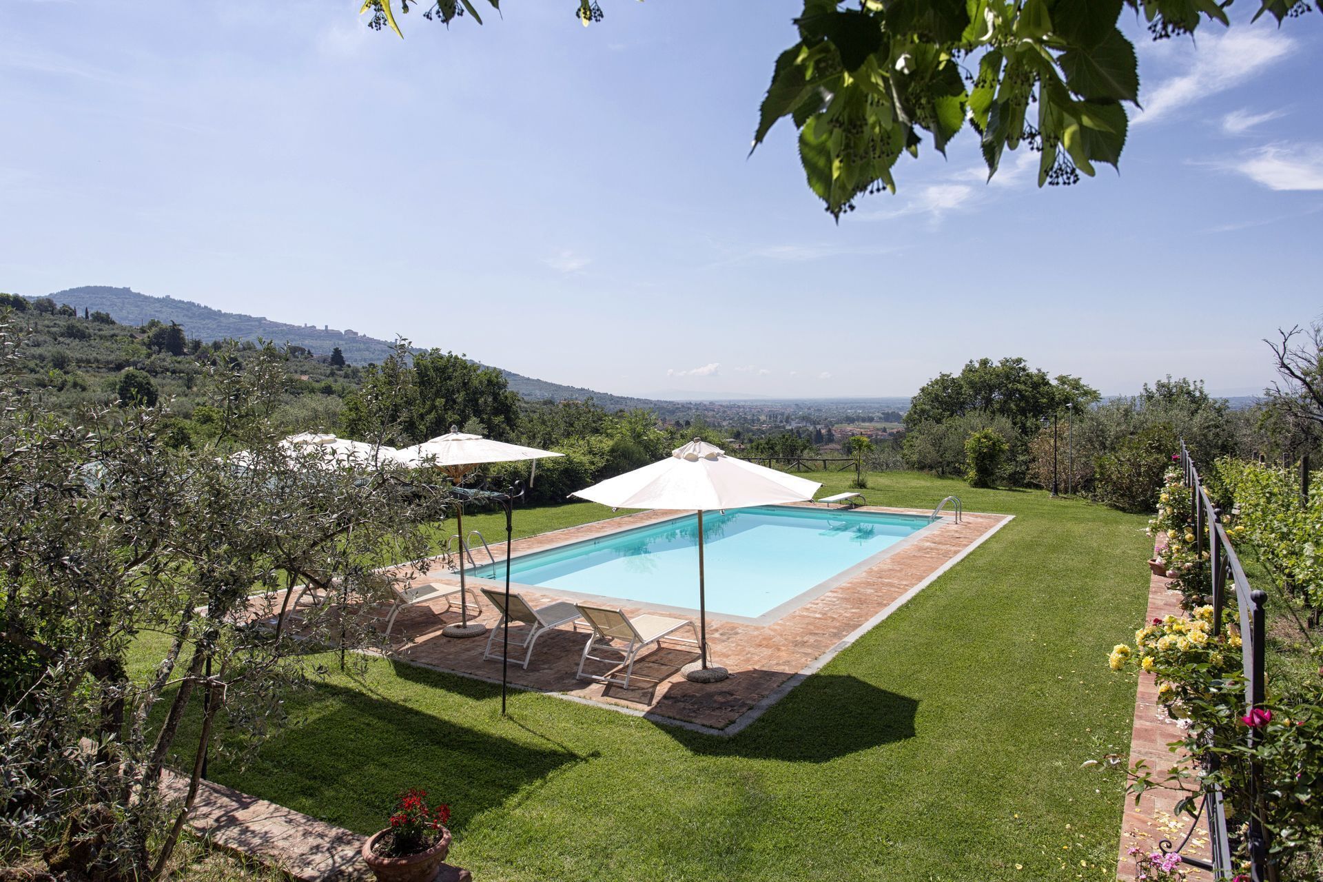 A rectangular swimming pool with a tiled deck, surrounded by a well-maintained lawn and two white umbrellas.