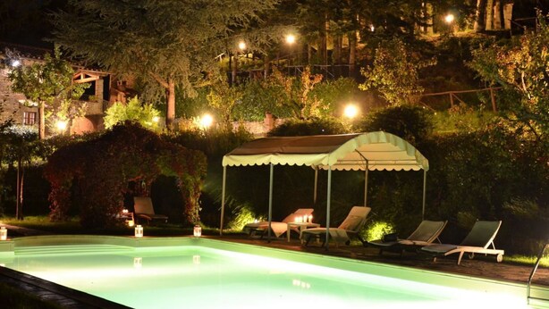 A nighttime swimming pool area with lounge chairs and a covered seating area, surrounded by trees and a building in the background. - Private Villa with private pool, WIFI, hot tub, A/C, TV, terrace, panoramic view, close to Cortona (Poggioni)