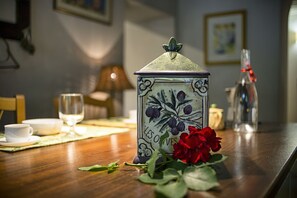 Uma mesa de jantar com um candeeiro cerâmico, uma garrafa de vidro e uma rosa vermelha.