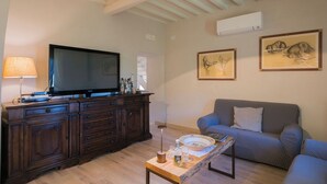 A living room with a television on a wooden cabinet, a grey sofa, and two framed artworks on the wall.