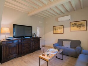 A living room with a television on a wooden cabinet, a grey sofa, and two framed artworks on the wall.