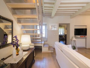 A modern living room with a staircase, a sofa, a television, and a dining area.