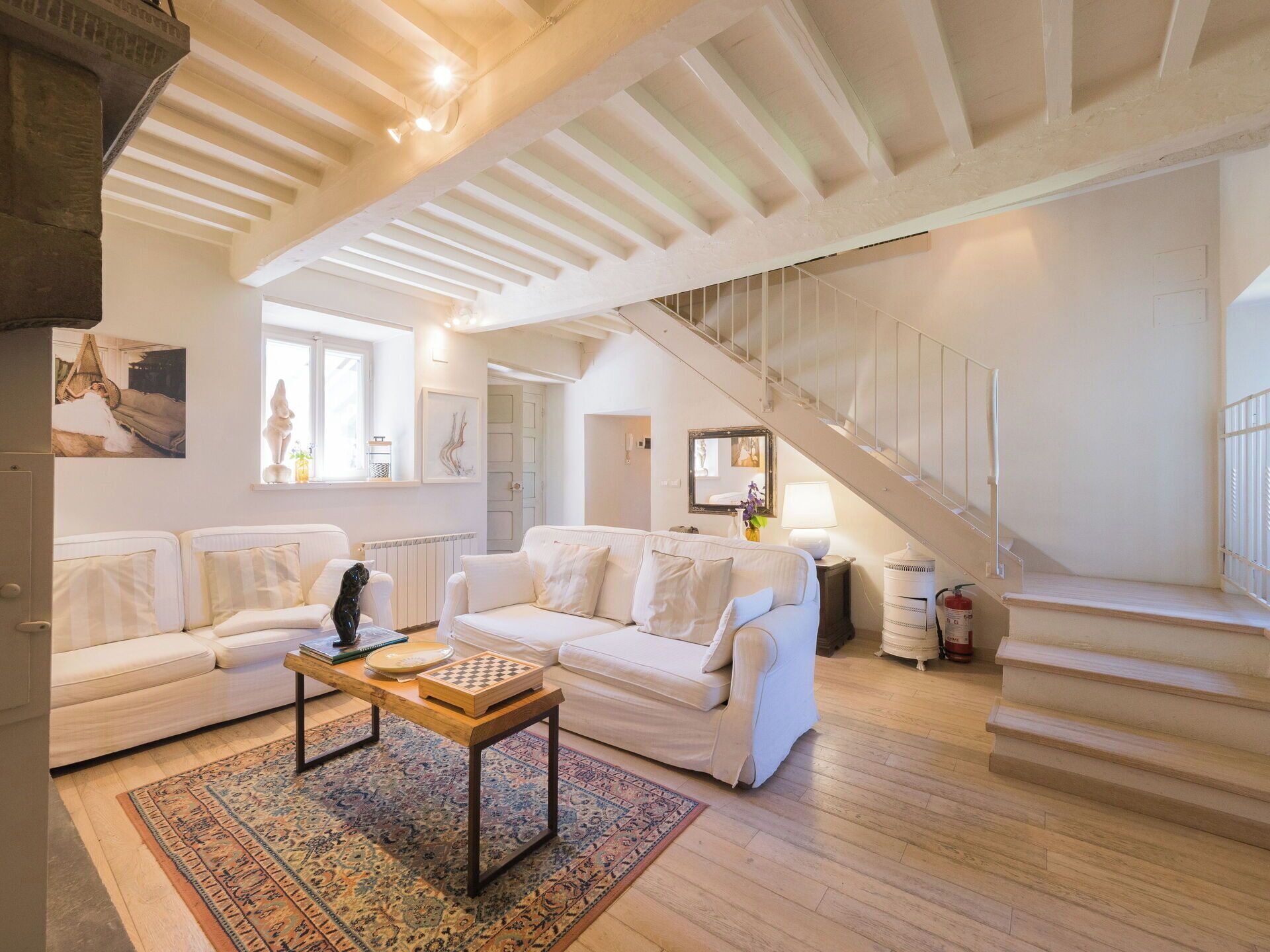 Un salón amplio con techo alto, sofás blancos, una mesa de centro de madera y una escalera.