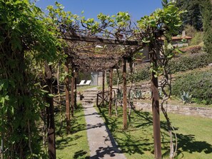 A garden pathway leading to a stone building with a pergola overhead.