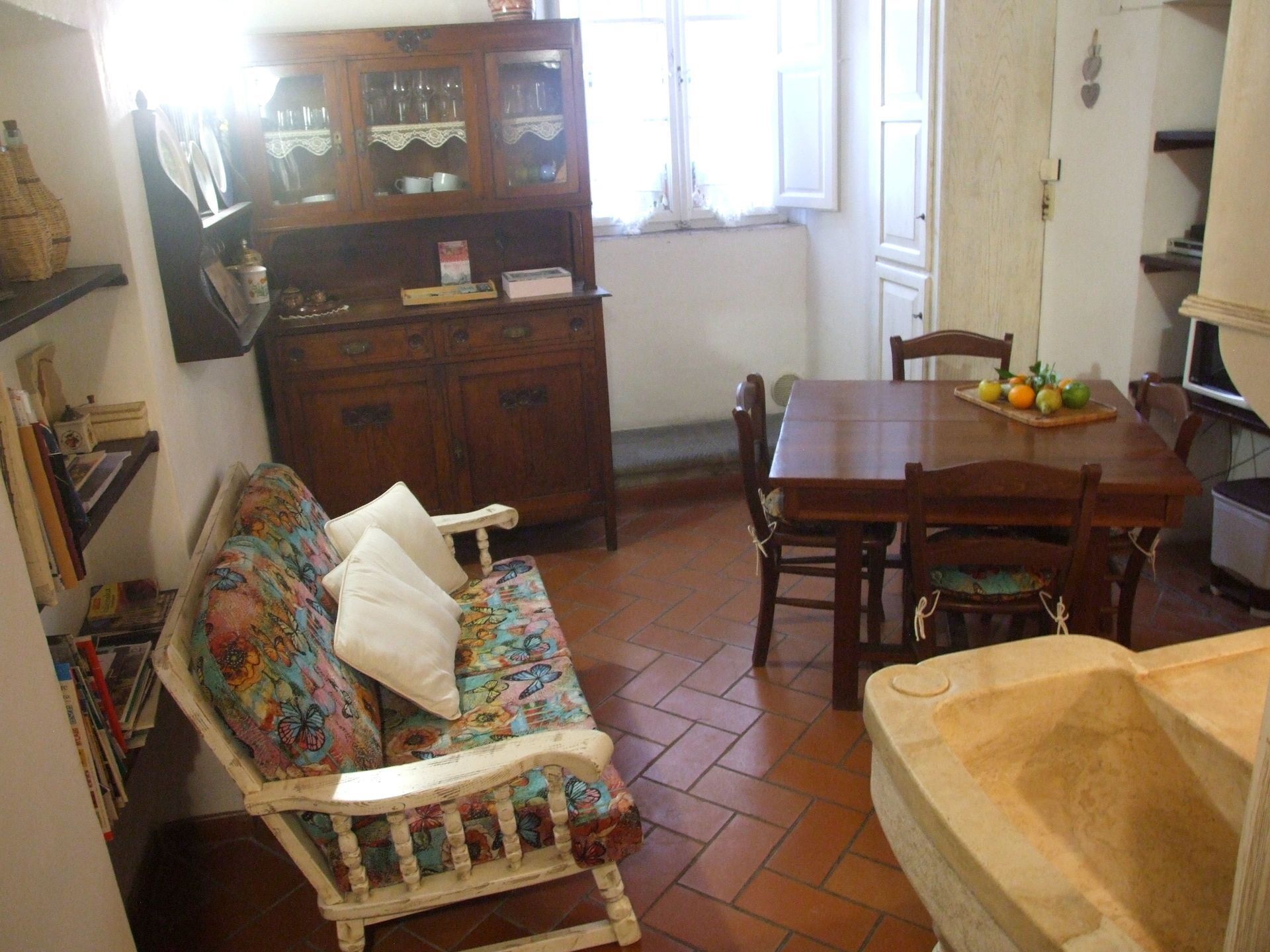 Una sala de estar acogedora con un sofá floral, una mesa de comedor de madera y un mueble bar con puertas de cristal.
