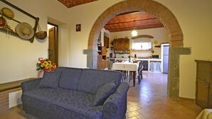 A cozy living room with a blue sofa, an arched brick ceiling, and a kitchen visible through the doorway. - Lovely apartment for 4 people with WIFI, A/C, TV and panoramic view (Cortona)