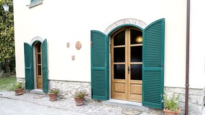 A building with two arched wooden doors with green shutters, a stone wall, and potted plants on the ground. - Lovely apartment for 4 people with WIFI, A/C, TV and panoramic view (Cortona)