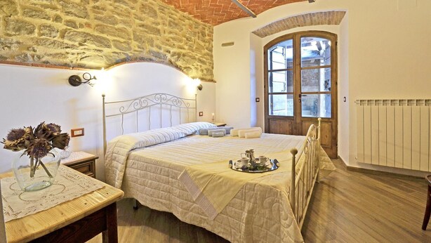 A bedroom with a stone wall, a wooden ceiling, a bed with a tray of tea, and a window with a view. - Lovely apartment for 4 people with WIFI, A/C, TV and panoramic view (Cortona)