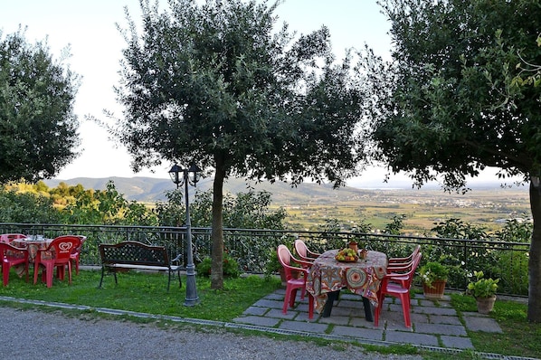 An outdoor seating area with a table and chairs, surrounded by trees and a view of the countryside.