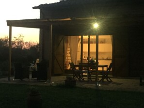 A covered outdoor dining area with a table and chairs, a fire pit, and a view of the interior through a glass door.