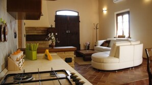 A living room with a sofa, a dining area with a table and chairs, a fireplace, and a kitchen with a stove. - Wonderful  villa for 4 guests with A/C, WIFI, private pool, TV and panoramic view, close to Cort... (La Villa-farneta)