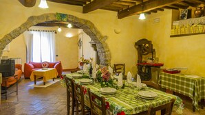 A dining area with a stone archway, wooden beams, and a table set for a meal.