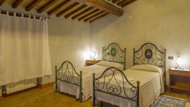 A bedroom with two single beds, a wooden ceiling, a stone floor, and a nightstand with a lamp. - Beautiful private villa for 9 guests with WIFI, private pool, TV, veranda and pets allowed (Cortona)