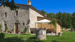 A stone building with a large open porch, potted plants, and a grassy lawn. - Beautiful private villa for 9 guests with WIFI, private pool, TV, veranda and pets allowed (Cortona)