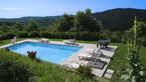 A rectangular swimming pool with lounge chairs and a table, surrounded by greenery and hills in the background. - Beautiful private villa for 9 guests with WIFI, private pool, TV, veranda and pets allowed (Cortona)