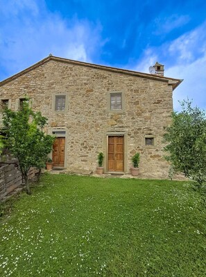 A stone building with a wooden door and windows, surrounded by a grassy lawn.