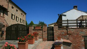 A courtyard with brick buildings, a wooden fence, and potted flowers. - Lovely apartment for 10 guests with pool, WIFI, TV and pets allowed (Camucia-monsigliolo)