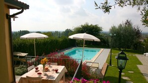 Zona junto a la piscina con una mesa, sillas y dos sombrillas, con vistas a la piscina.