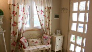 Una habitación acogedora con una cama, una mesita de noche, un armario y una ventana con cortinas florales.