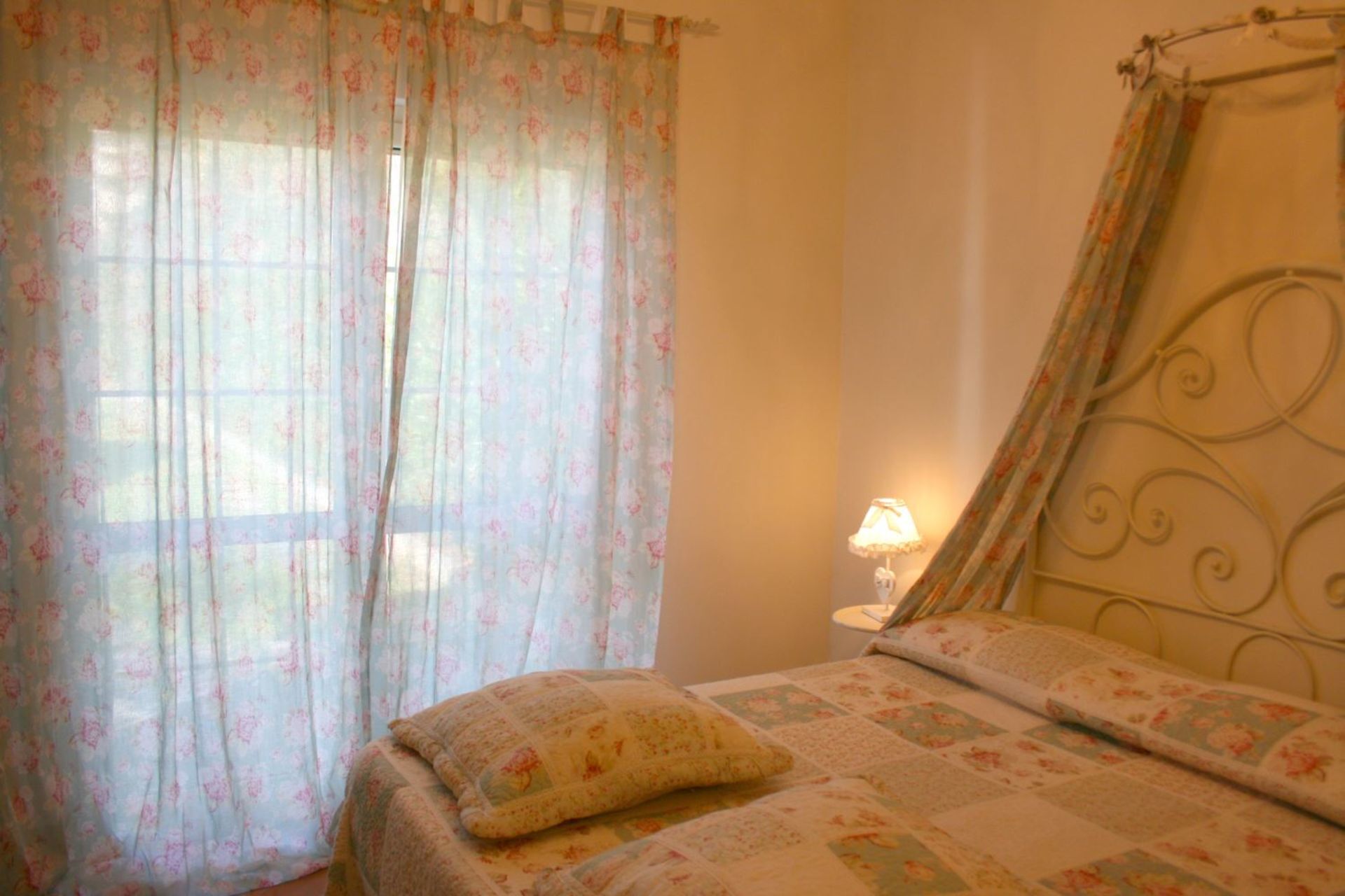 Ein Schlafzimmer mit blumigen Vorhängen, einem Bett mit floraler Bettdecke und einer Nachttischlampe.