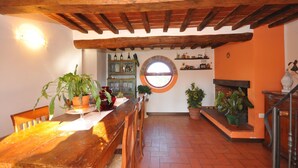 A rustic interior with a wooden dining table, chairs, a fireplace, and a window overlooking a garden. - Wonderful private villa with A/C, private pool, WIFI, TV and panoramic view, close to Cortona (Montecchio)