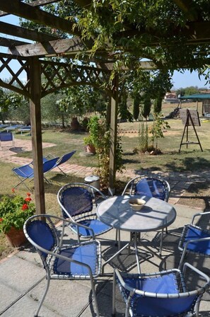 An outdoor patio with metal chairs and a table, surrounded by a wooden pergola and greenery.