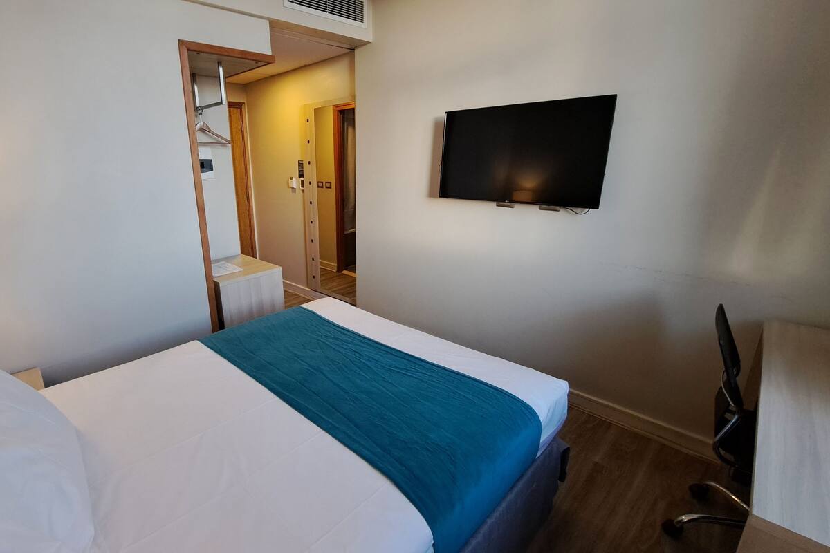 Habitación de hotel con una cama, un escritorio, una silla, un televisor montado en la pared y una puerta que da al baño.