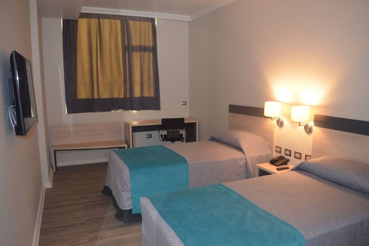 Habitación de hotel con dos camas, un escritorio, una silla, un televisor y dos lámparas de noche.