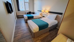 A hotel room with two beds, a desk, a chair, a TV, and a window with curtains.