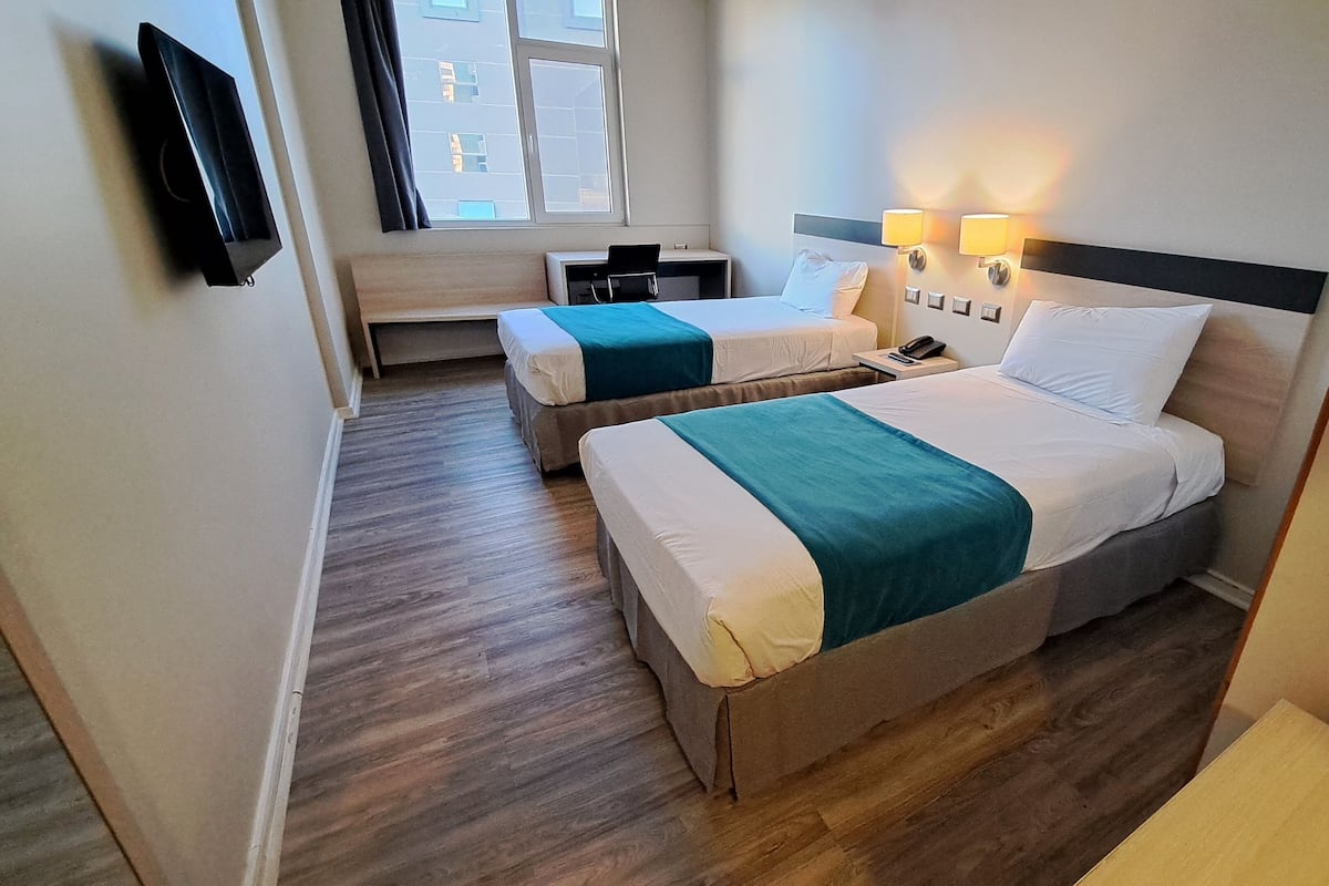Habitación de hotel con dos camas, un escritorio, una silla, un televisor y una ventana con cortinas.