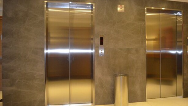 Two elevator doors in a modern building with a marble wall.