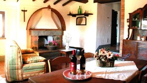 A cozy living room with a stone fireplace, wooden beams, and a dining table set with bottles and flowers. - Cosy apartment for 6 guests with WIFI, pool, A/C and TV (Camucia-monsigliolo)