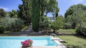 Una piscina con borde de piedra y una maceta con flores rosas en primer plano.