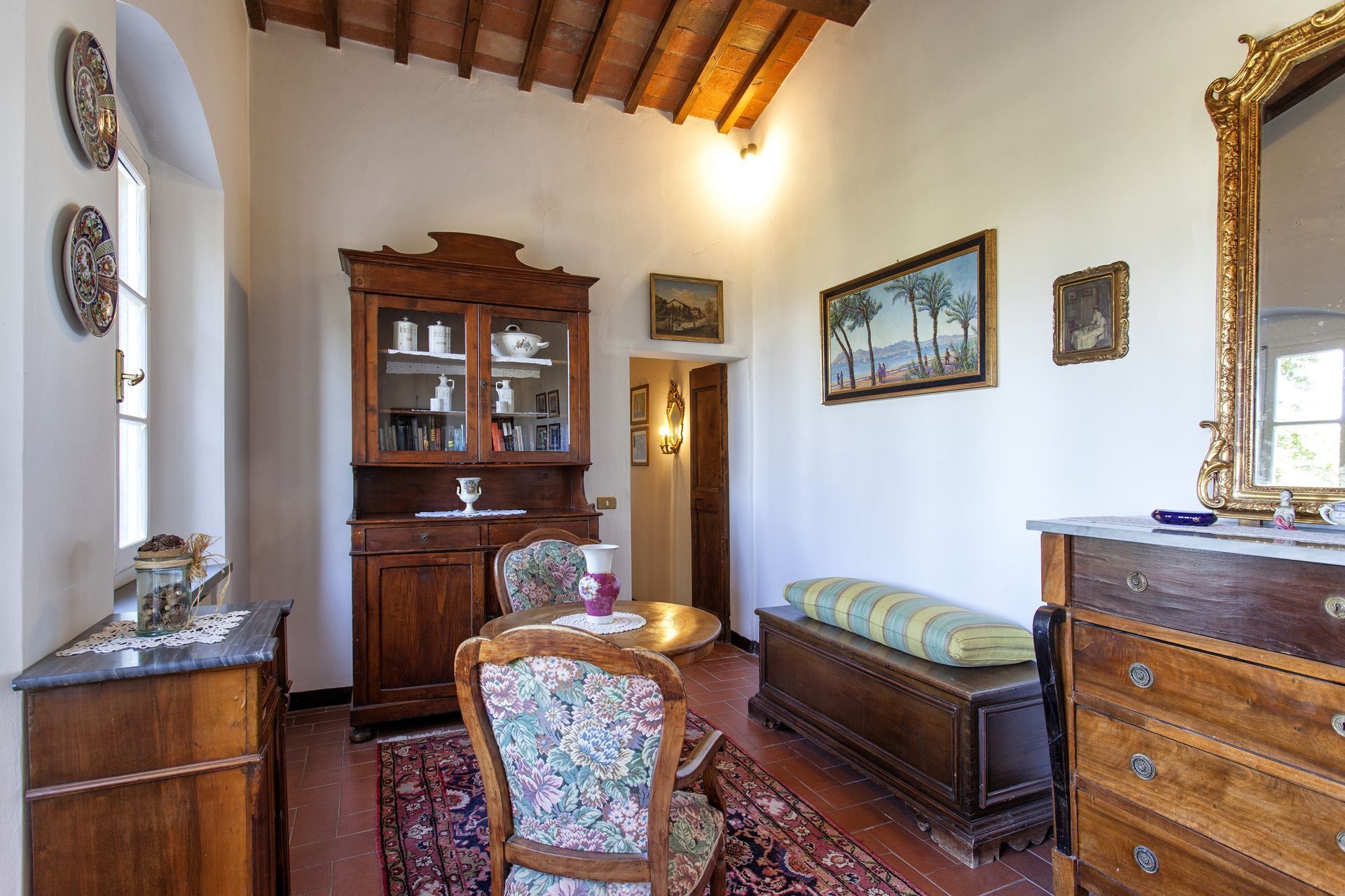 Une pièce au décor traditionnel, avec un meuble en bois, un fauteuil à motifs floraux, un banc et un miroir.