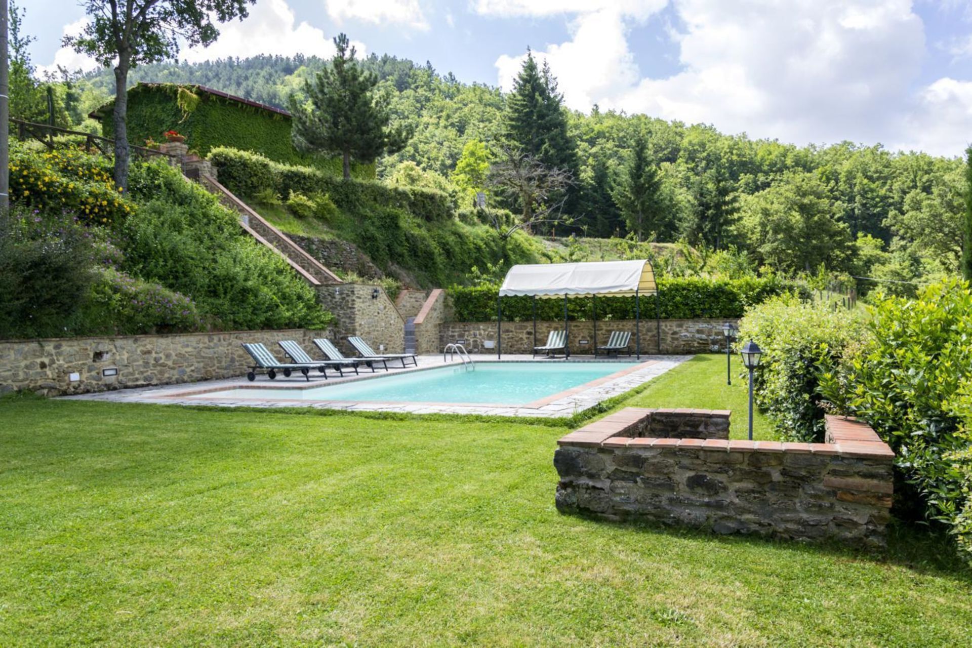 A swimming pool with lounge chairs, surrounded by a stone wall and lush greenery.