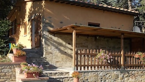 A rustic stone house with a wooden porch, potted flowers, and a small table. - Stunning private villa for 4 people with WIFI, private pool, TV, terrace and panoramic view (Cortona)