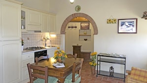 A kitchen with white cabinets, a wooden dining table, and a brick archway leading to another room. - Stunning private villa for 4 people with WIFI, private pool, TV, terrace and panoramic view (Cortona)