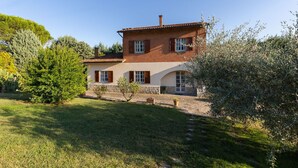 A two-story house with a tiled roof, stone foundation, and a small garden with various plants and trees.