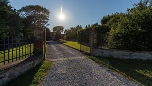 A gravel pathway leading to a gated entrance with stone walls and a metal fence.