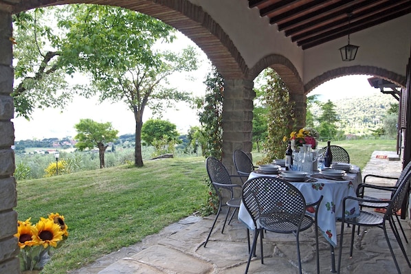 An outdoor patio with stone flooring, metal chairs, and a table set for dining.