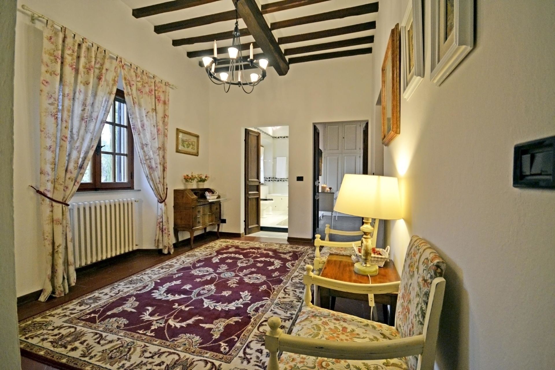 Una habitación con techo de madera, un candelabro, un tapete estampado, una silla y una mesa con lámpara.
