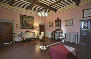 A room with a wooden ceiling, a large painting, a sofa set, a table, and a red bedspread.