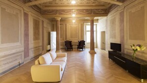 Una habitación amplia con piso de madera en espiga, un sofá blanco, dos sillones, un mueble de entretenimiento negro y un gran ventanal con luz natural.