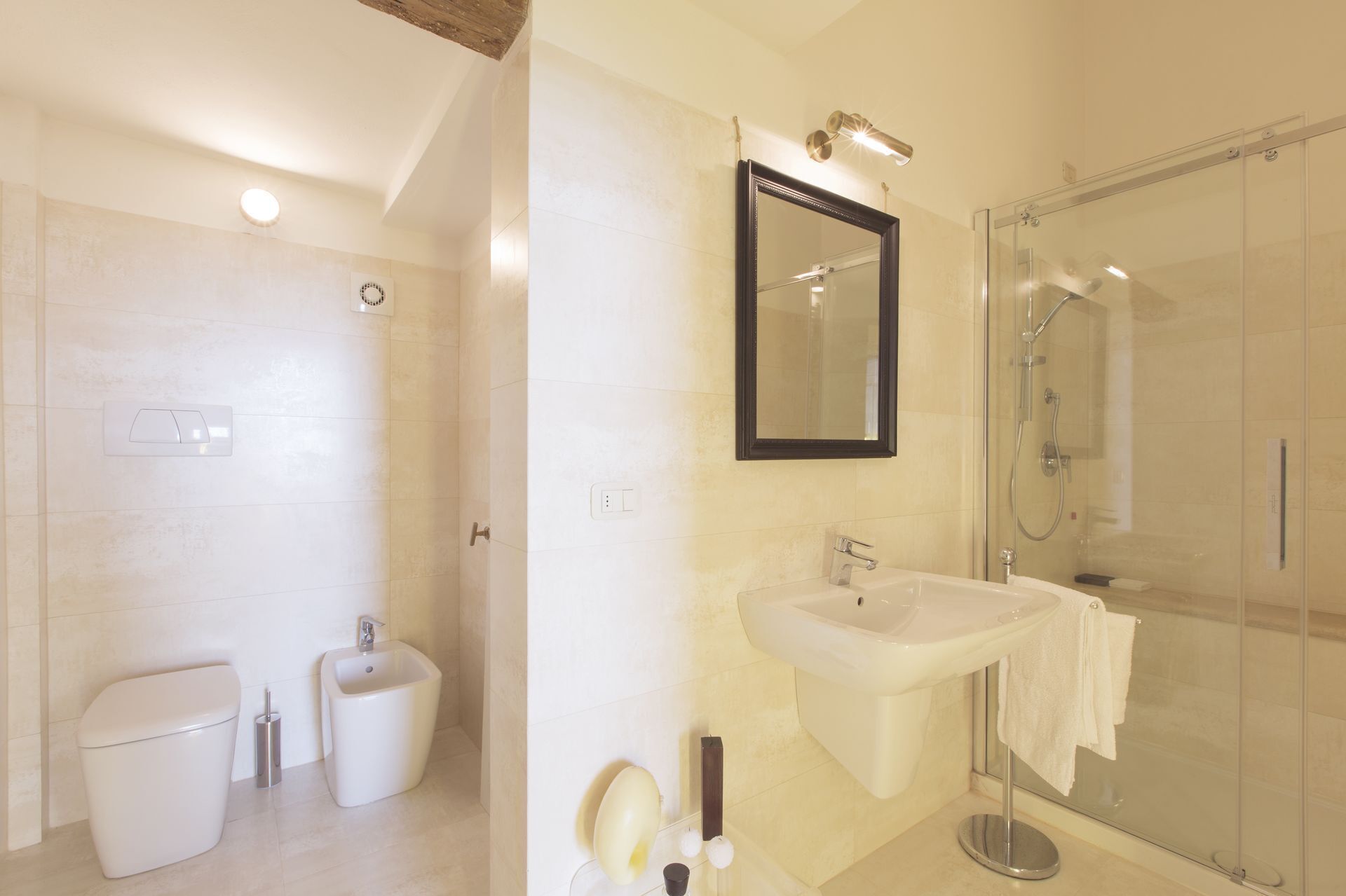 A modern bathroom with a toilet, bidet, sink, and glass-enclosed shower.
