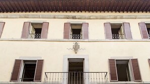 Un edificio con fachada de piedra, una entrada central con puerta de madera y varias ventanas con contraventanas.