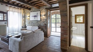 A cozy living room with a stone wall, a white sofa, and a wooden ceiling. - Private Villa with hot tub, A/C, sauna, WIFI, pool, TV, terrace, panoramic view, close to Cortona (Torreone)