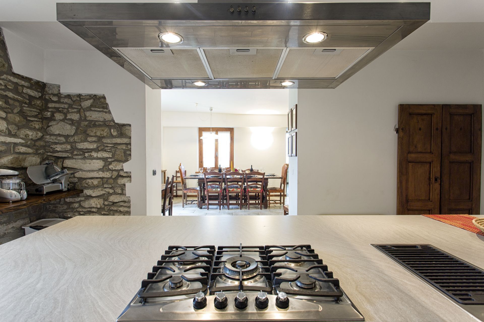 A kitchen with a gas stove, a stone wall, and a dining area with wooden chairs and a table.